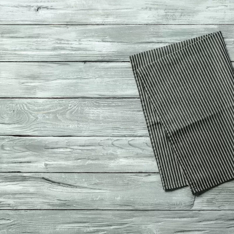 Gray wooden table with balck and white dark linen kitchen towel or textile napkin flat lay. Dark tablecloth on old gray wood tabletop. Copy space for text. Can use as mock up for design.